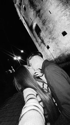 black and white photograph of two people kissing in front of an old building at night