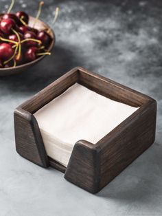 a wooden box with napkins in it next to a bowl of cherries on a table