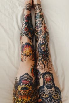 tattooed legs laying on top of a white bed covered in sheets and pillows with tattoos