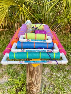 a wooden pole with many different colored tubes on it and some plants in the background