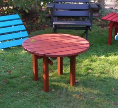 three different colored wooden chairs and table in the grass with one sitting on it's side