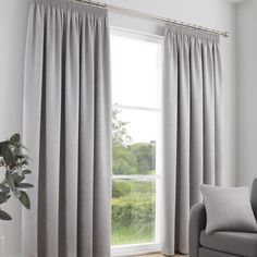 a living room with a couch, chair and large window covered in light blue curtains