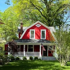 a red house with white trim on the front porch and covered in grass, surrounded by trees