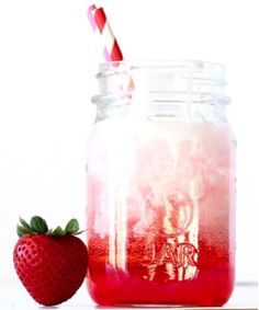 a strawberry sitting next to a mason jar filled with liquid and a straw in it