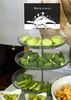 three tiered trays filled with vegetables and crackers next to bowls of fruit