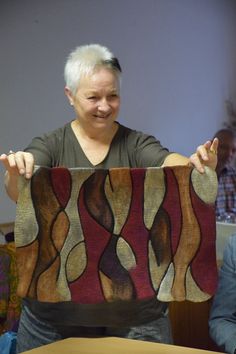 an older woman holding up a piece of art in front of her face while sitting at a table