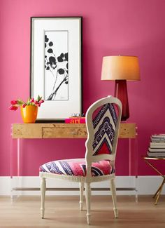 a chair and lamp in front of a pink wall with flowers on the table next to it