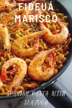 a pan filled with pasta and shrimp on top of a table next to a knife