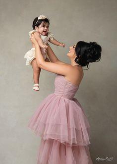 a woman in a pink dress holding a baby up to her face and smiling at the camera