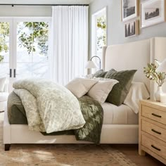 a white bed sitting in a bedroom next to a window filled with curtains and pillows