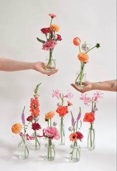 several vases with flowers in them being held by two hands