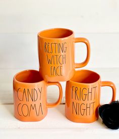 three orange coffee mugs with writing on them sitting next to each other and a black object