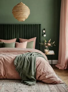 a bedroom with green walls, pink bedding and a hanging light over the headboard