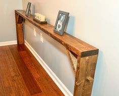 a wooden shelf with two pictures on it in the corner of a room next to a hardwood floor