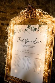 a wedding seating sign is lit up with fairy lights