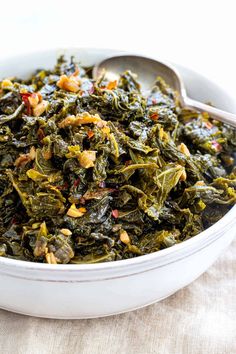 a white bowl filled with greens and nuts on top of a table cloth next to a spoon