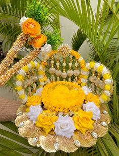 yellow and white flowers are arranged in a basket on a table with palm tree leaves