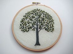 a small embroidered tree with green leaves on it's hoop hanging from a wall