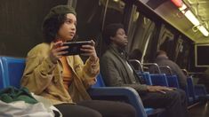 two people sitting on a train looking at their cell phones while one person sits in the passenger seat