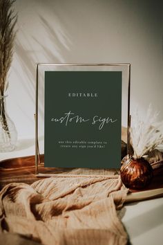 an empty sign sitting on top of a table next to a vase with dry grass