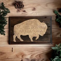 a wooden bison cutout on a wall next to pine cones and evergreen branches,