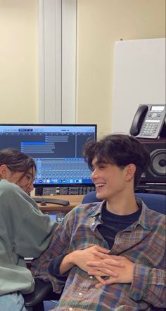 two young men sitting in front of computer monitors, one smiling and the other looking at something