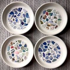 four white bowls with different colored sea glass in them sitting on a gray tablecloth