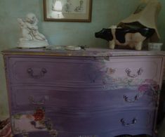 a purple dresser with an angel figurine sitting on top of it next to a cow statue