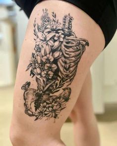 a woman's thigh with flowers and a skeleton tattoo on the side of her leg