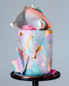 a multicolored cake with icing and decorations on a black stand against a gray background