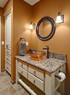 a bathroom with an oval mirror and marble counter top, along with white cabinetry