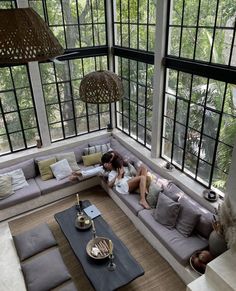 a woman laying on top of a gray couch in a living room next to large windows