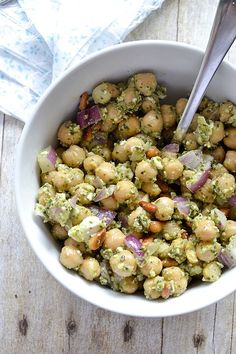 a white bowl filled with chickpeas and broccoli on top of a wooden table