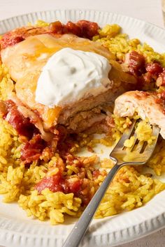 a white plate topped with rice and meat covered in sauces next to a fork