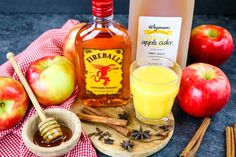 an apple cider, cinnamon sticks and apples on a table