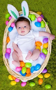 a baby is laying in a basket with easter eggs around it and wearing bunny ears