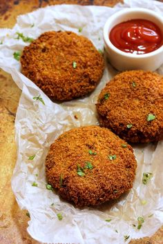 three fried food items sitting on wax paper with ketchup and sauce in the background