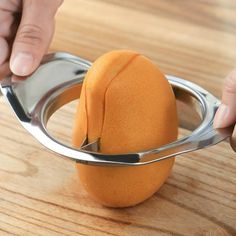 a person holding a metal spoon over an orange on a wooden table