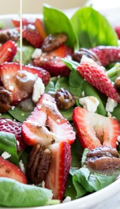 spinach salad with strawberries and nuts being drizzled with dressing