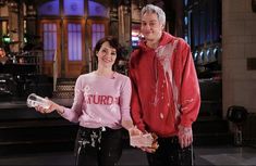 a man and woman standing next to each other in front of a tv screen with paint all over them