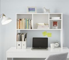 a laptop computer sitting on top of a desk next to a white book shelf filled with books