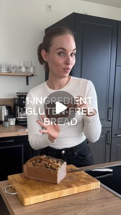 a woman standing next to a loaf of bread on top of a wooden cutting board