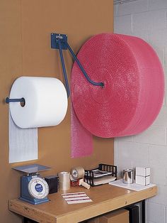 a pink hat hanging on the wall next to a roll of toilet paper