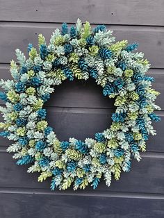 a wreath made out of pine cones and green leaves hanging on a wall with wood planks in the background