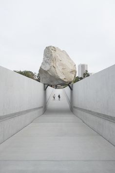 two people walking down a walkway with a large rock in the middle