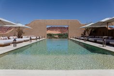 an outdoor swimming pool with lounge chairs and umbrellas on the side, in front of a desert - like building