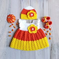 a crocheted dress, hat and booties are laying on a white wooden surface