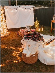 an outdoor picnic is set up with lights and blankets on the grass, while two small trees are in the background