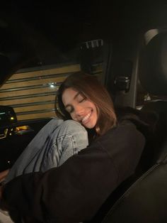 a woman sitting in the passenger seat of a car smiling and looking at the camera