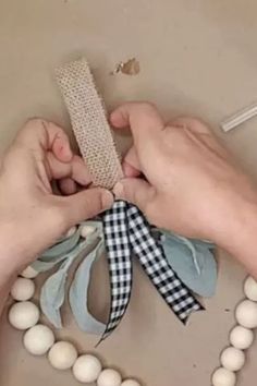 two hands are tying a ribbon around a beaded bracelet